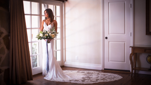 bride with bouquet stands in front of window with beautiful smile Westlake Village Inn