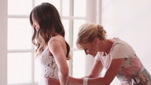 Mother helping bride lace up dress