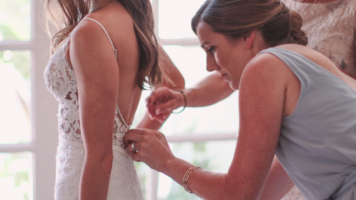 Mother and sister helping bride button up dress