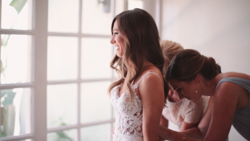 Mother and sister helping bride button up dress