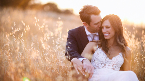 Bride and groom smiling and sitting in a field at sunset Brookview Ranch Malibu